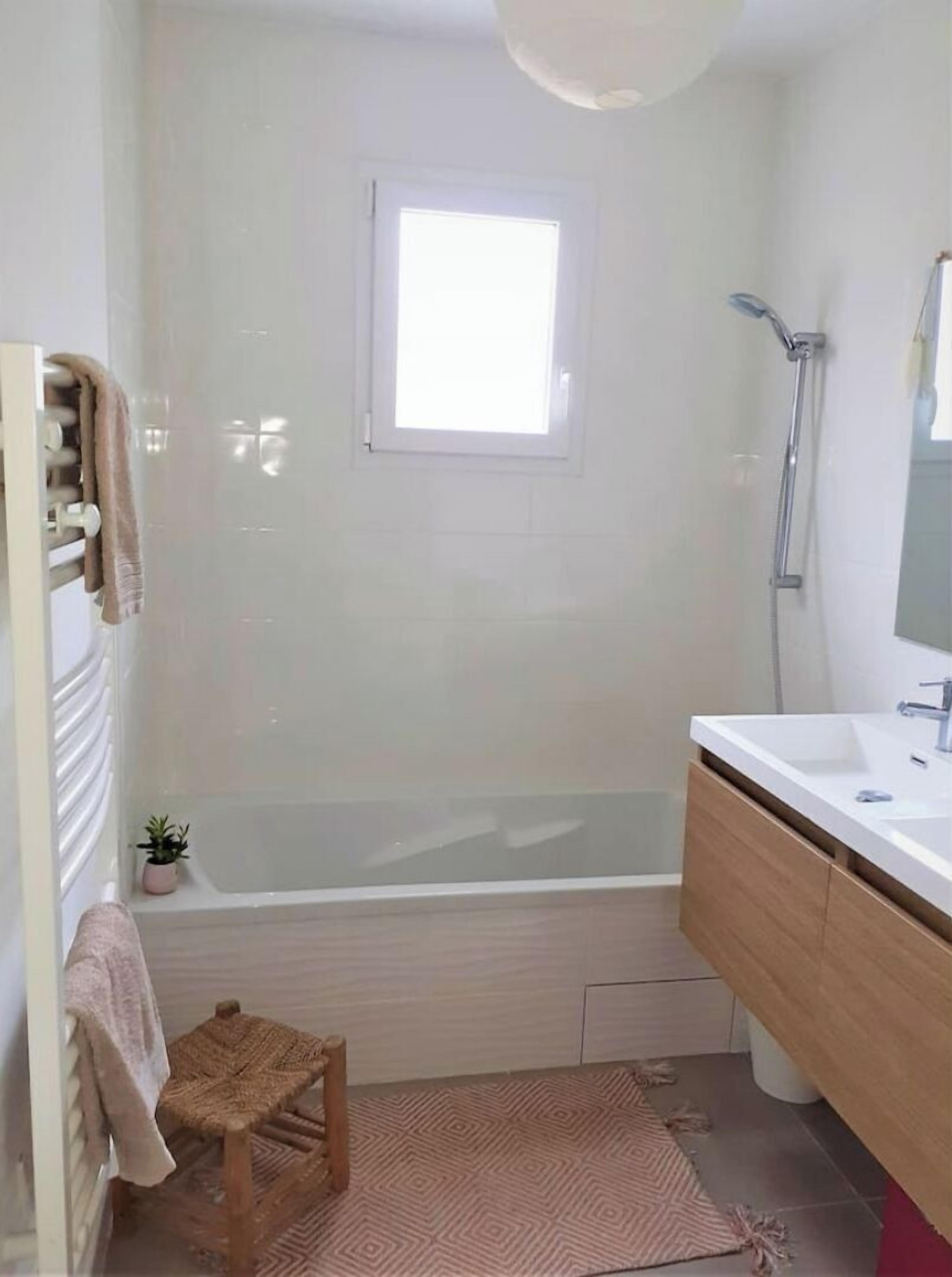 A bathroom with a bathtub, a shower, a sink, and a small stool.