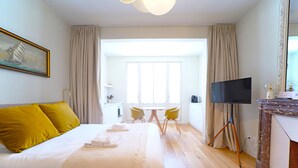 A hotel room with a bed, a TV, a desk, and a window. - Villa Adèle, Escapade Belle-Époque - Appt 01 (Mers-les-Bains)
