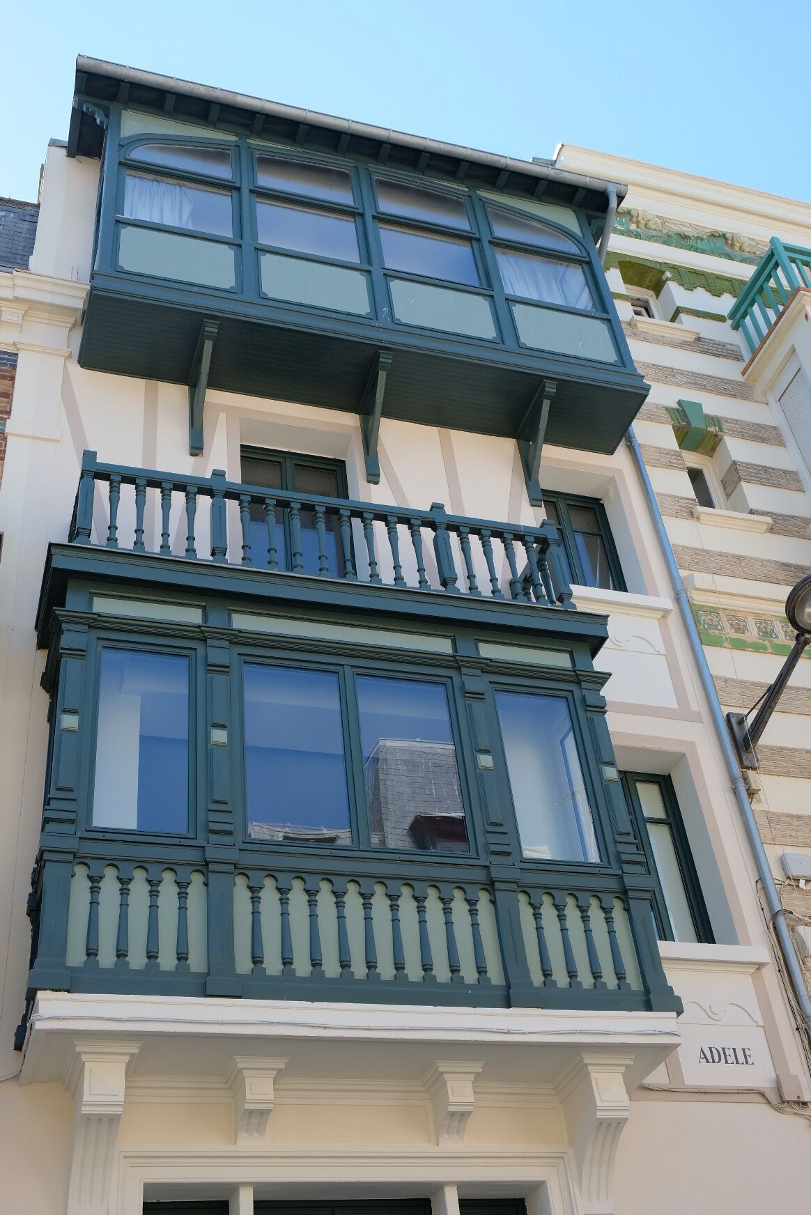 A multi-story building with a balcony on the second floor and a nameplate reading "ADELE".