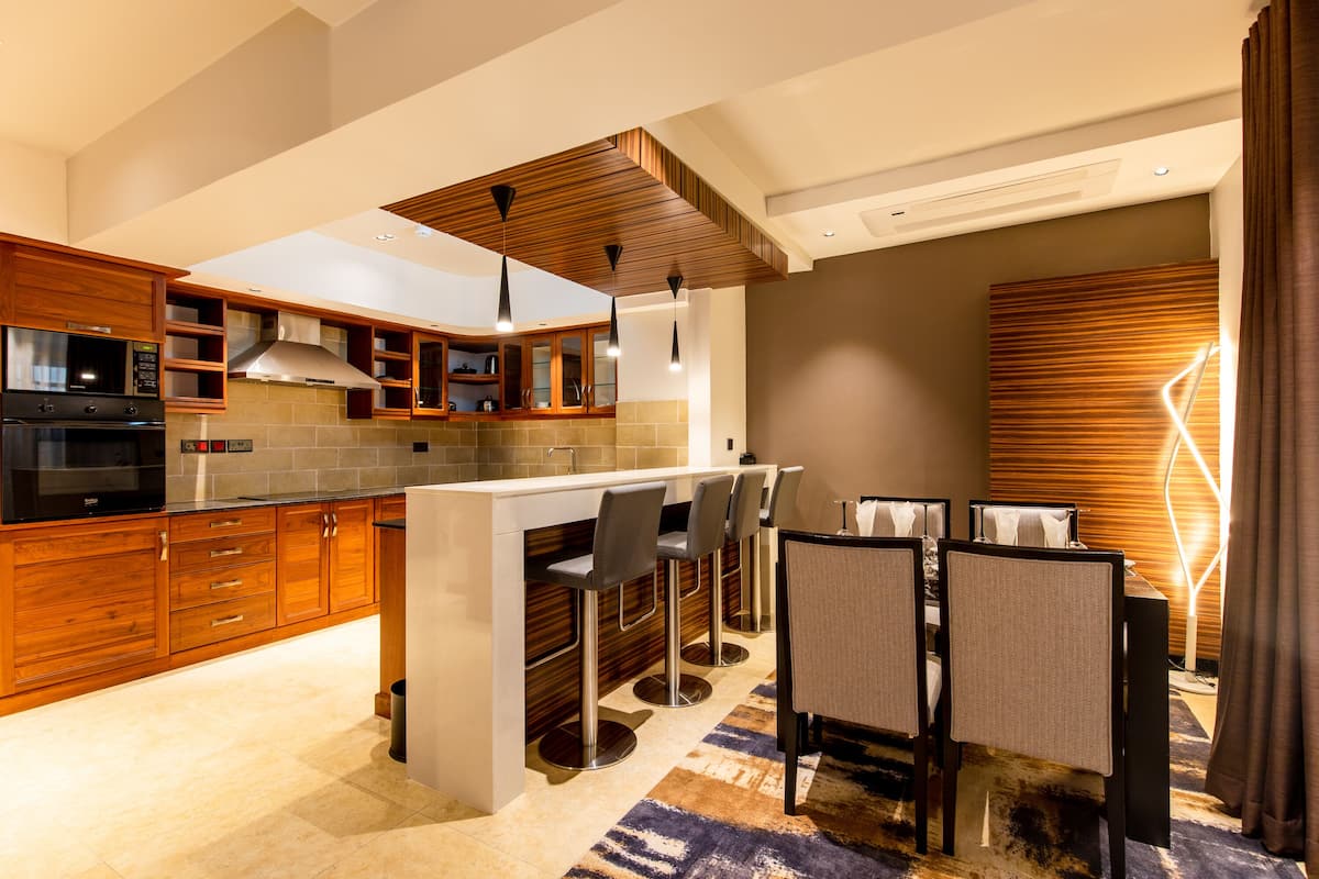 A modern kitchen with wooden cabinets, a built-in microwave, and a bar area with stools.