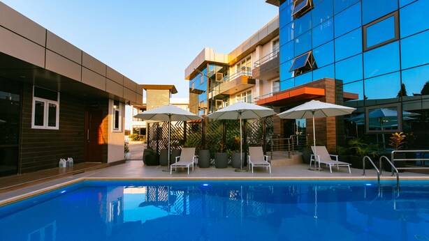 A modern hotel with a swimming pool, lounge chairs, and umbrellas. - Blackwood Hotel and Apartments (Dar es Salaam)