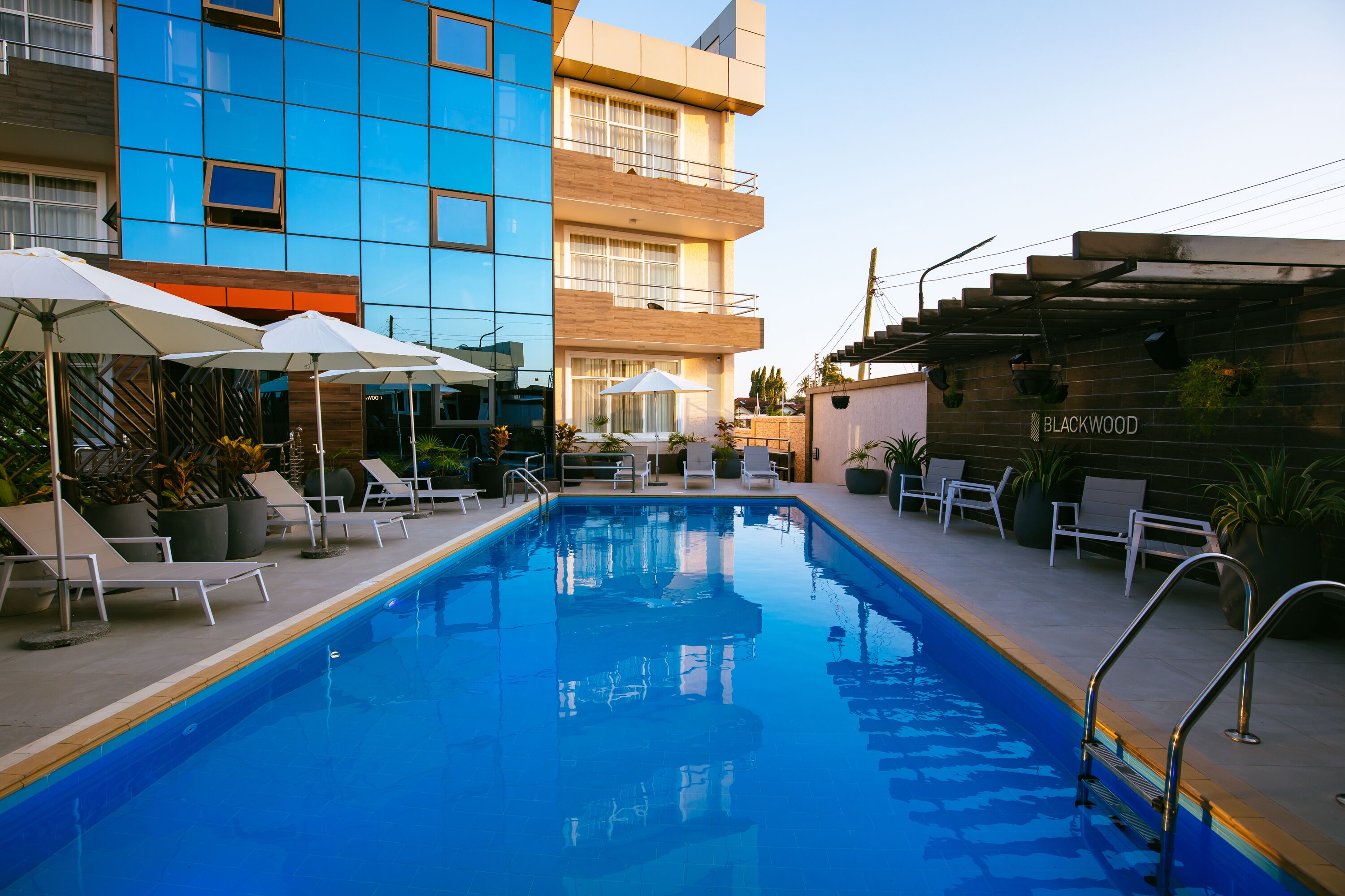 A swimming pool with lounge chairs and umbrellas, surrounded by modern buildings.
