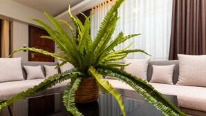 A fern plant in a brown pot on a glass coffee table in a modern living room with a beige sofa and light-colored cushions. - Blackwood Hotel and Apartments (Dar es Salaam)
