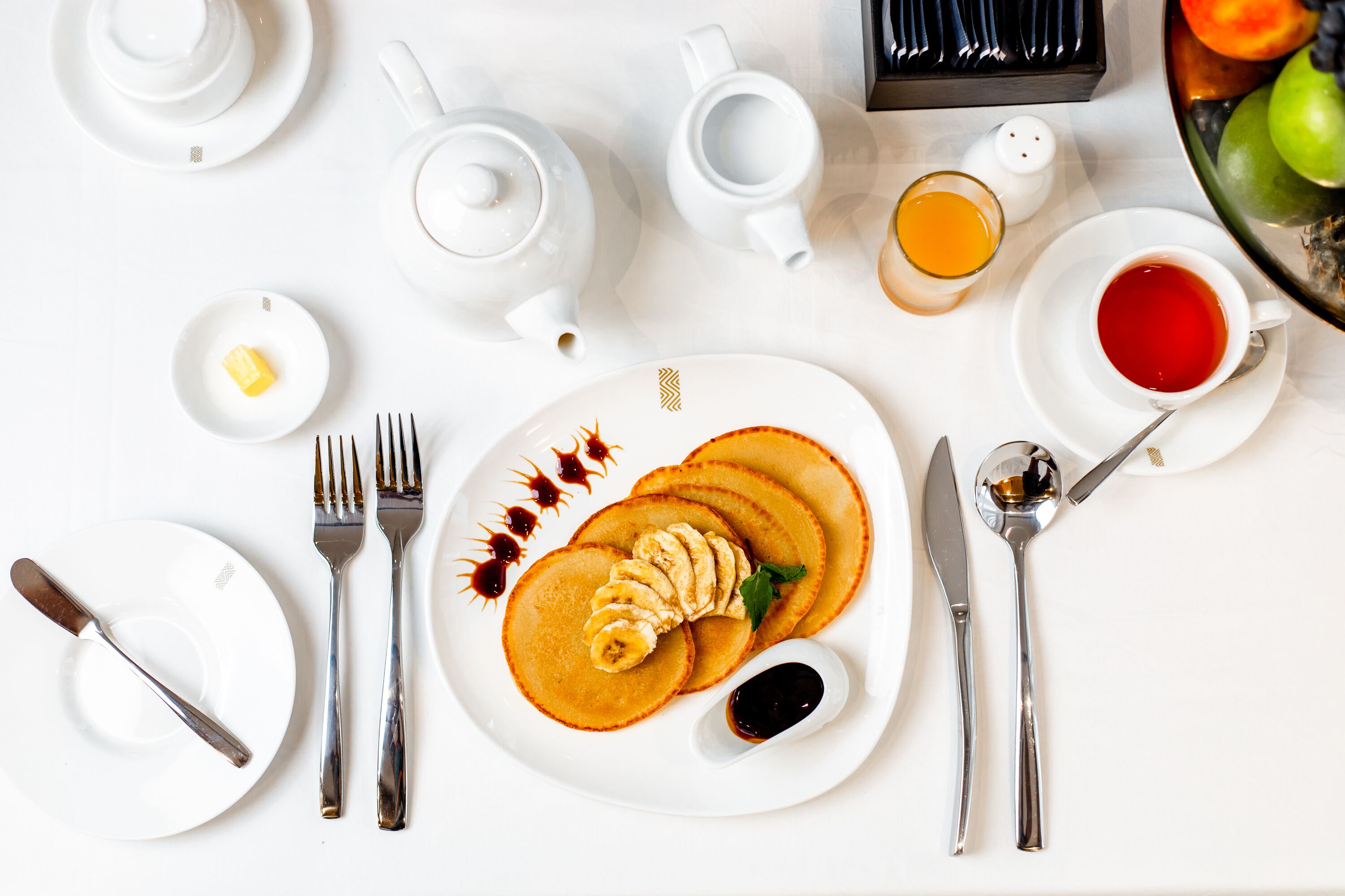 A breakfast setting with pancakes, butter, syrup, and a fruit bowl.