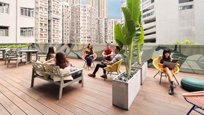 A rooftop terrace with seating, a large potted plant, and a view of high-rise buildings. - Weave Studios - Olympic (Kowloon)