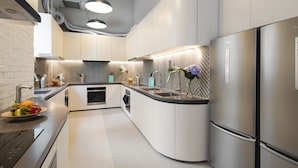 A modern kitchen with a curved island, stainless steel appliances, and a herringbone tile backsplash. - Weave Studios - Olympic (Kowloon)