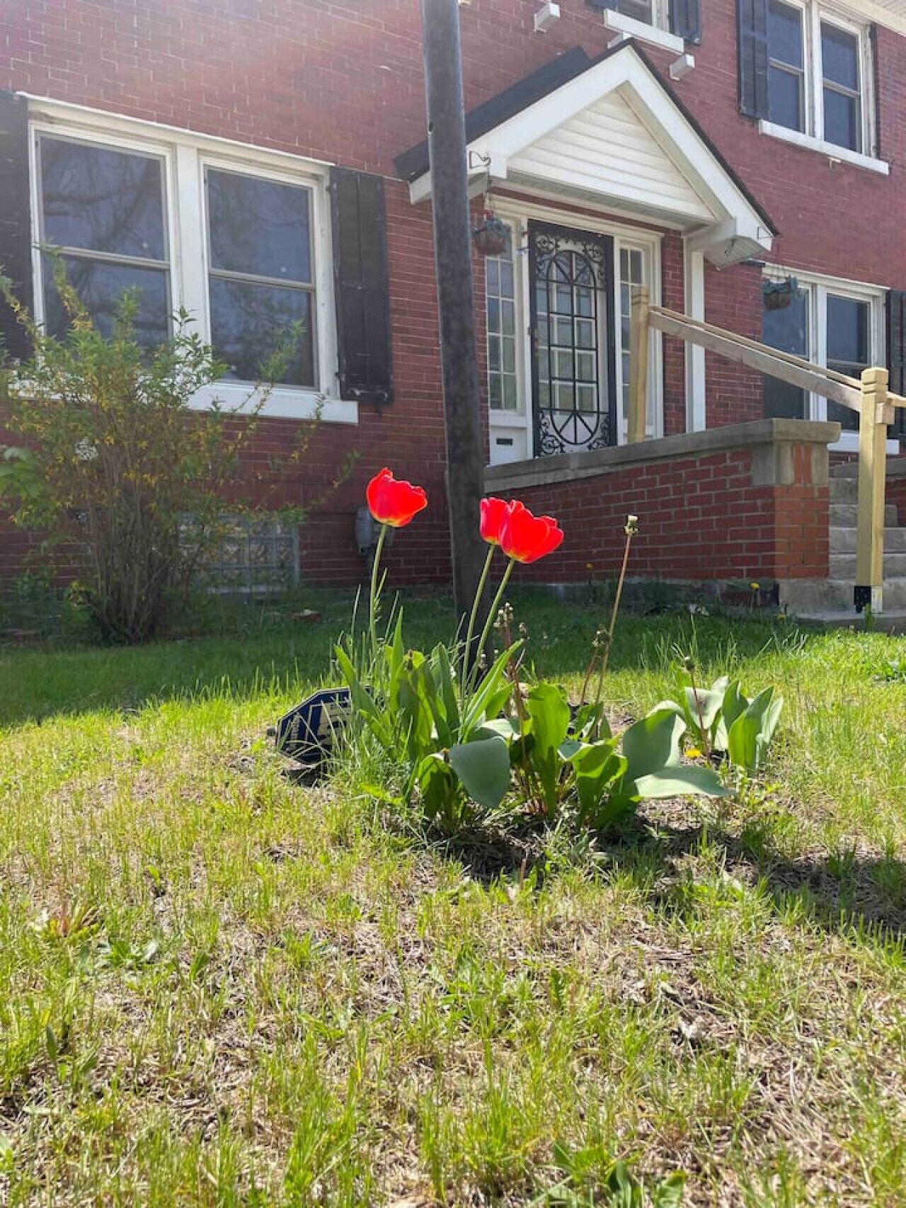 Una casa con fachada de ladrillo, un porche delantero y un pequeño jardín con flores rojas y plantas verdes.
