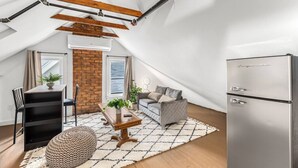 Un appartement de style « loft » avec des poutres apparentes, un mur en briques, un coin repas avec une table et des chaises, un canapé, un tapis et un réfrigérateur.