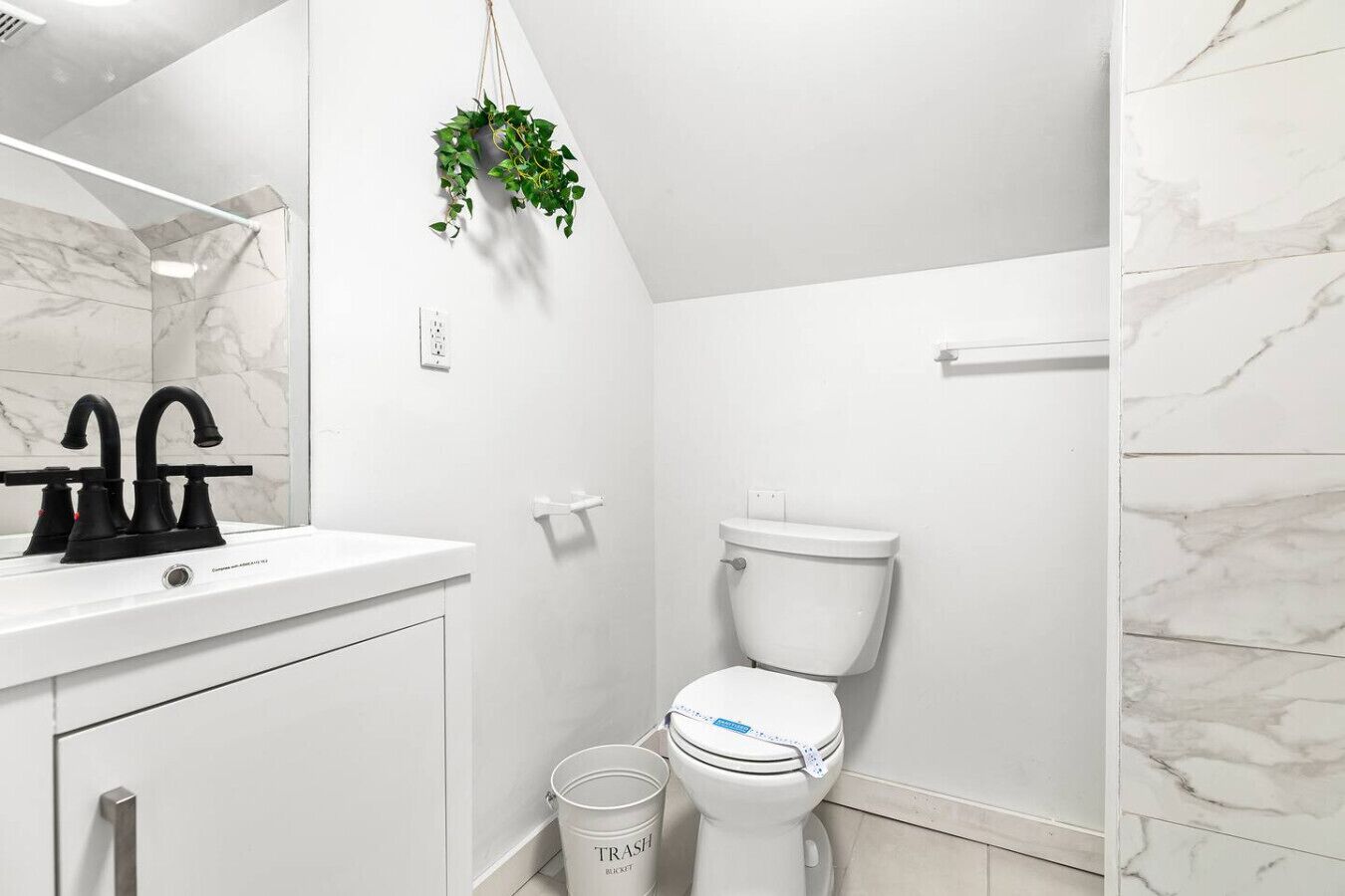 A bathroom with a white sink, black faucet, white toilet, and a trash can.