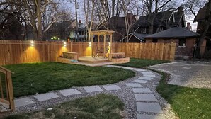 Un jardin avec une terrasse en bois, une pergola et un chemin en pierre.