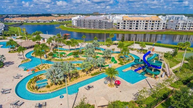 An aerial view of a resort with a large swimming pool, palm trees, and a water slide.