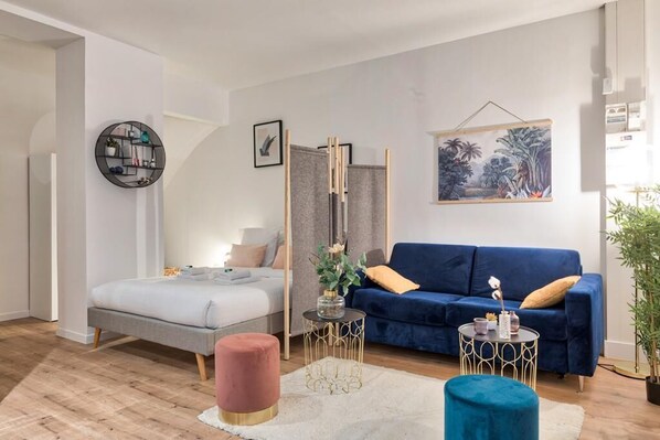 A modern bedroom with a bed, a blue sofa, a round side table, and a painting on the wall.
