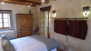 Een slaapkamer met een houten deur, een radiator, een bed met kussens en gordijnen met een patroon.
