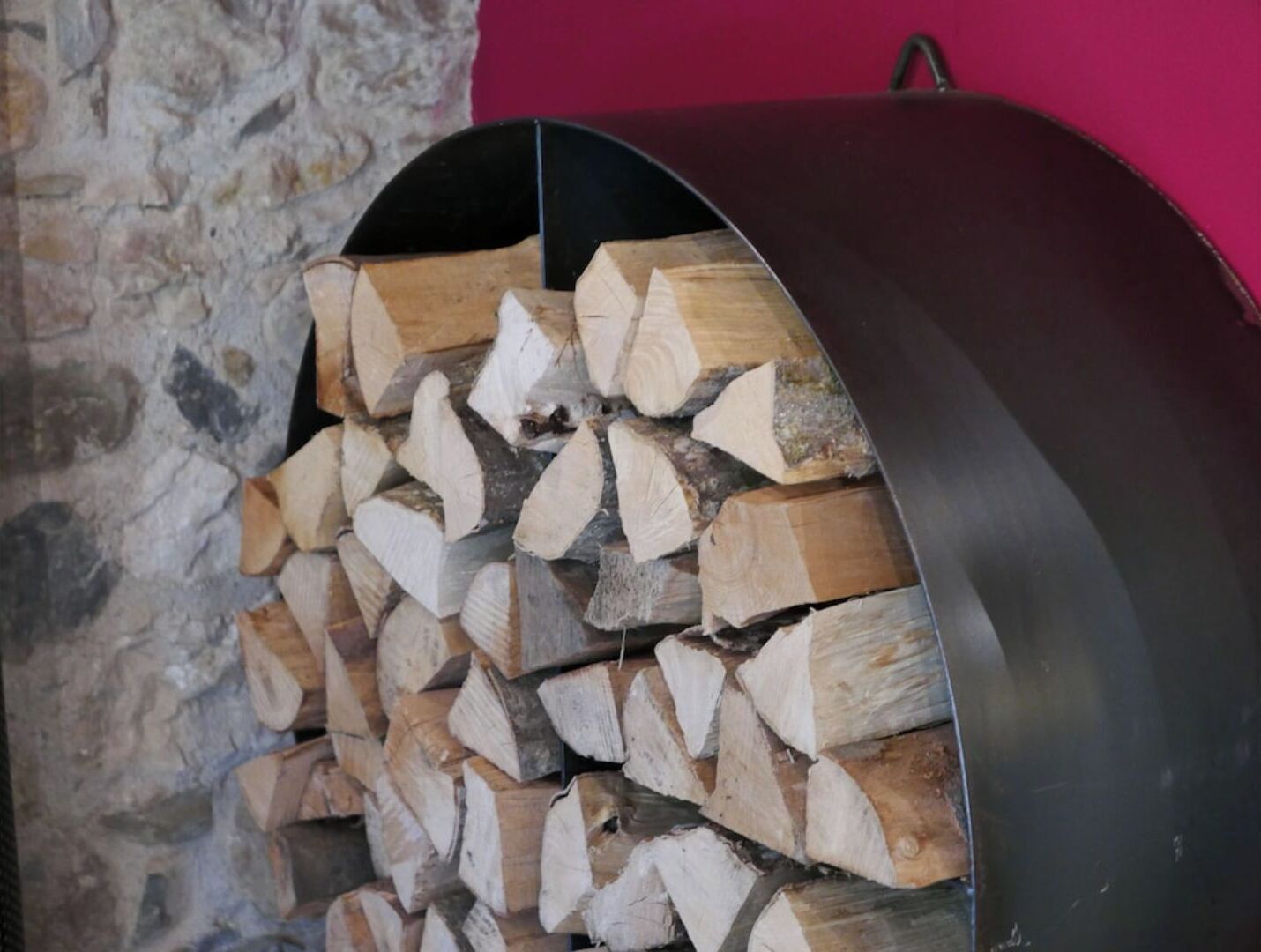 Een stapel houtblokken in een metalen haard, met een stenen muur en een roze muur op de achtergrond.