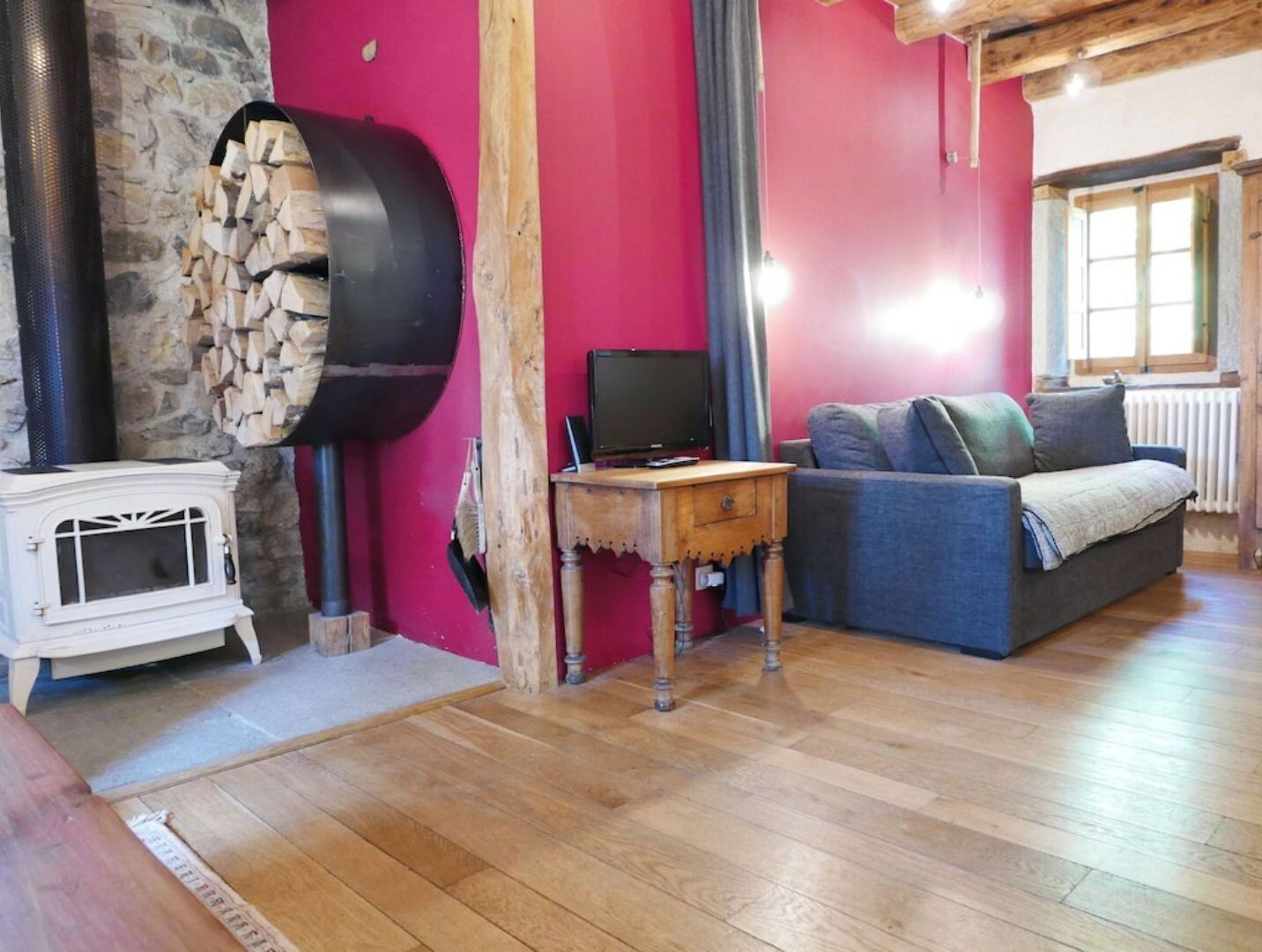 A cozy living room with a stone wall, a wood-burning stove, a grey sofa, and a small wooden table.