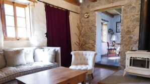 A cozy living room with a wooden table, a sofa, a white armchair, and a stone wall.