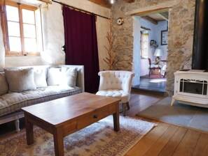 Una sala de estar acogedora con una mesa de madera, un sofá, un sillón blanco y una pared de piedra.