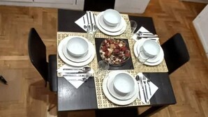Una mesa de comedor preparada con platos, tazones y cubiertos, rodeada de sillas.