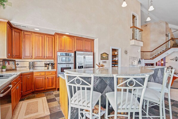 Cocina con armarios de madera, encimera de granito y una isla central con taburetes de bar.