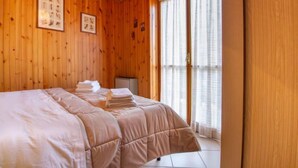 Ein Zimmer mit Holzwandverkleidung, einem Bett, einem kleinen Tisch und einem Fenster mit Vorhängen.