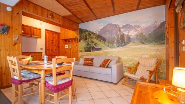 Ein gemütliches Holzinnere mit Essbereich, Sofa und einer Wandmalerei von einer Berglandschaft.