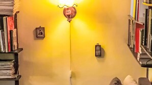 Una habitación con una pared amarilla, una estantería, una lámpara y un marco de fotos.