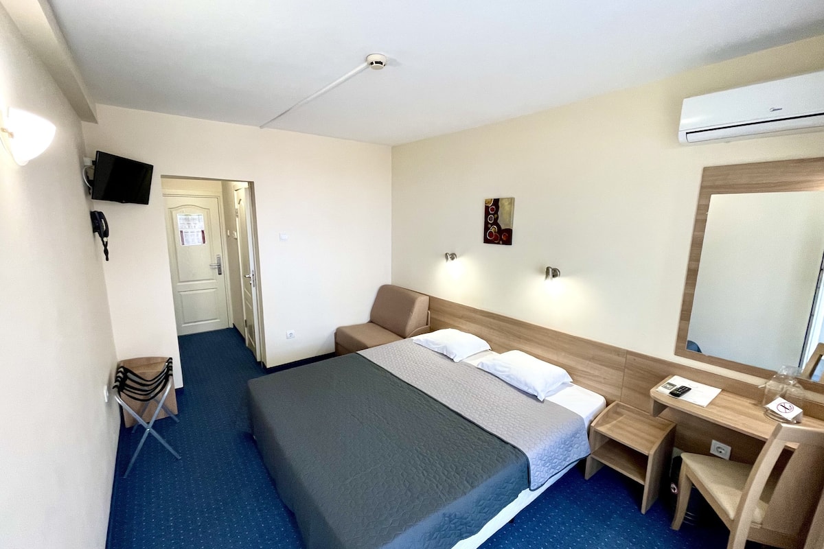 A hotel room with a bed, bedside table, chair, desk, and a large mirror.