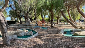 Ein Park mit baumgesäumten Wegen, einem kleinen Teich und Steinbauten.