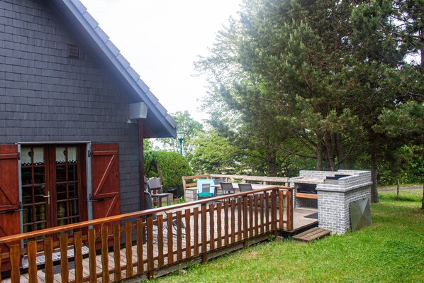 A house with a wooden deck, a brick barbecue area, and a large tree in the background.