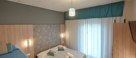 Una habitación de hotel con dos camas, un cabecero de madera, una lámpara en el techo y una ventana con cortinas.