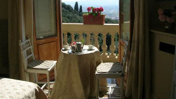 Ein Balkon mit Tisch für zwei Personen, Stühlen, einem Blumentopf und Blick auf die Landschaft.