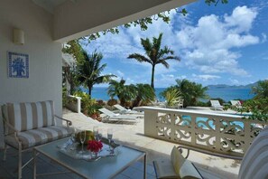 A balcony with a view of the sea, a sofa, a table with glasses and flowers, and a decorative fence.