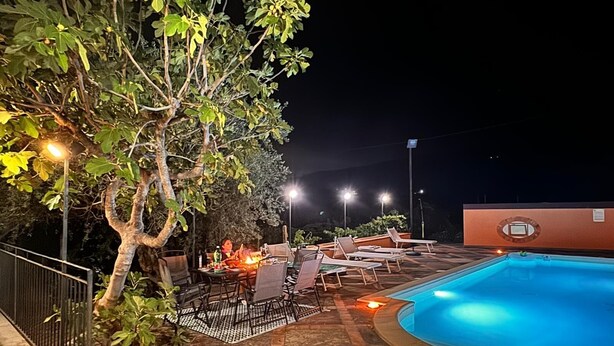 Ein Poolbereich im Freien mit Liegestühlen und einem Tisch, umgeben von einer Steinterrasse und einem Baum.