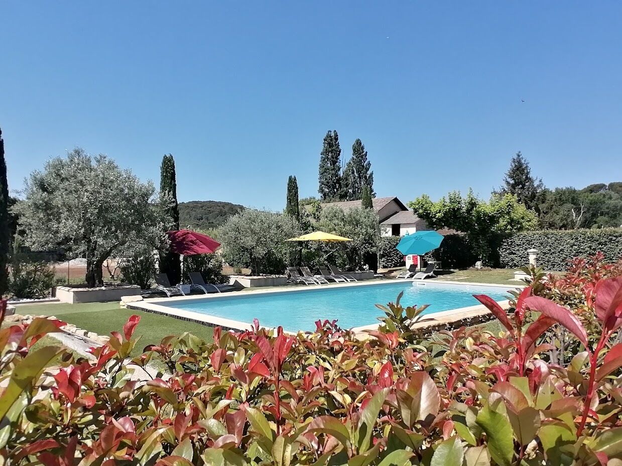 A swimming pool with sun loungers and umbrellas, surrounded by lush greenery and trees.