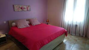 Un dormitorio con cama, mesita de noche, lámpara y ventana con cortinas.
