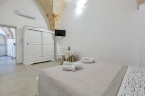 A bedroom with a large bed, a wardrobe, a TV mounted on the wall, and a bathroom visible through an archway.