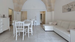 A spacious living area with a dining set and a sofa, a kitchen in the background, and a high arched ceiling. - 3063 Dimora Ilenia by Barbarhouse (Oria)