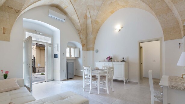 A spacious living area with a dining table and chairs, a sofa, and an open kitchen area with a fridge and cabinets. - 3063 Dimora Ilenia by Barbarhouse (Oria)