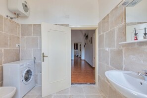 Ein Badezimmer mit einer Waschmaschine, einem Waschbecken und einer Tür zu einem Flur.