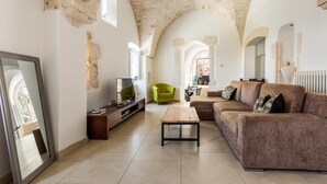 Ein geräumiges Wohnzimmer mit einer hohen, gewölbten Decke, einem Holztisch, einem braunen Sofa und einem grünen Sessel.