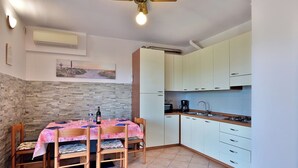 Eine kleine Küche mit weißen Schränken, einem Esstisch mit Blumenmuster und einem Deckenventilator.