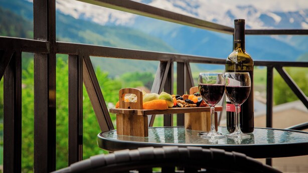 A table with a bottle of wine and glasses, a fruit tray, and a mountain view. - Chalet Mestia (Mestia)