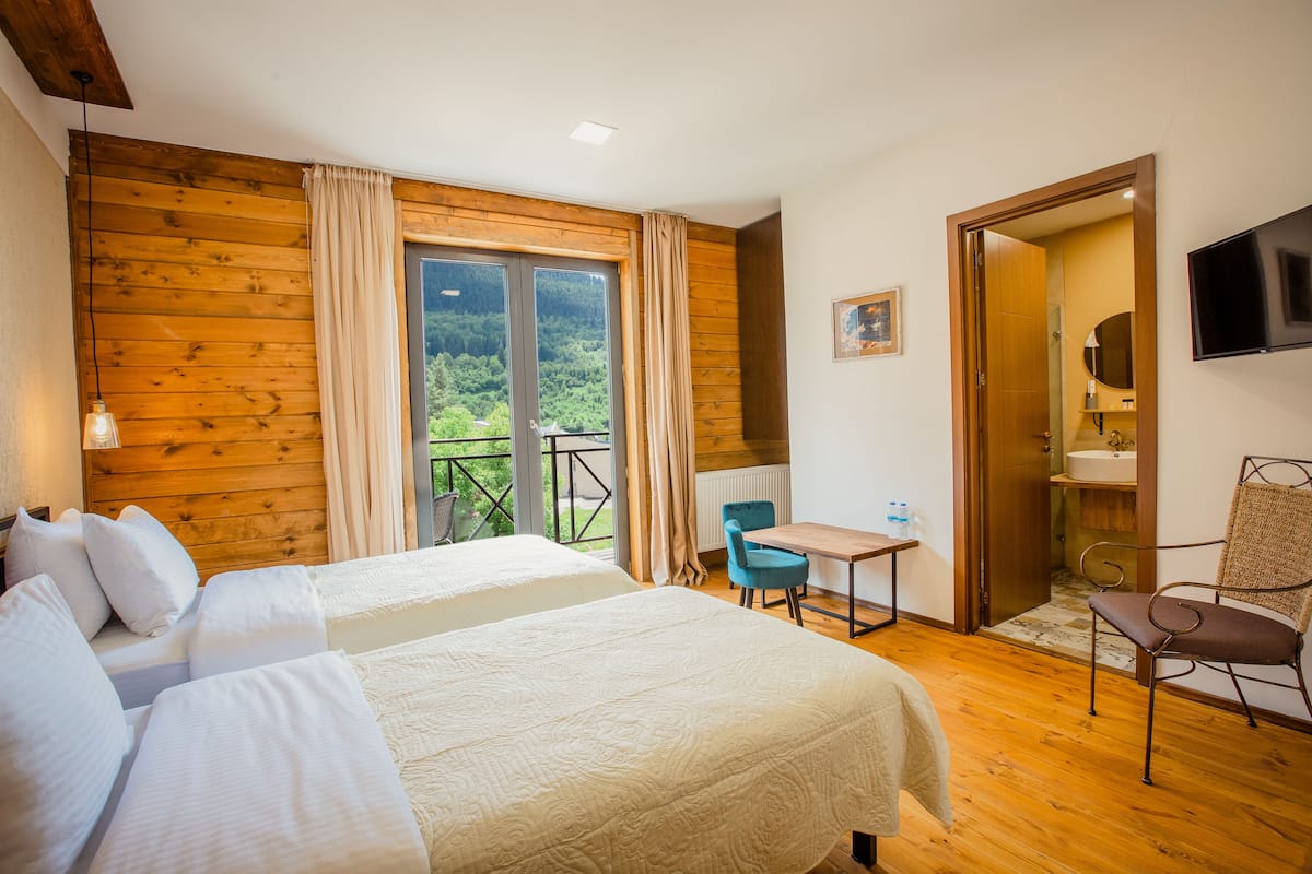 A bedroom with two beds, a desk, a chair, a TV, and a view of the outdoors.