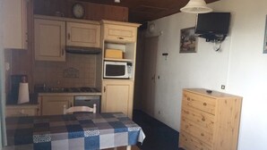A compact kitchen with wooden cabinets, a microwave, a sink, and a dining table with a checkered tablecloth. - Arette: Large studio for 6 near slopes, parking, dishwasher (Arette)