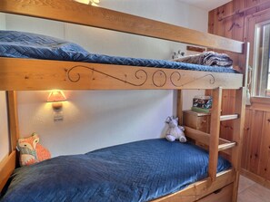 Cozy bunk bed room with a blue quilted mattress, wooden headboard, and a shelf for personal belongings.