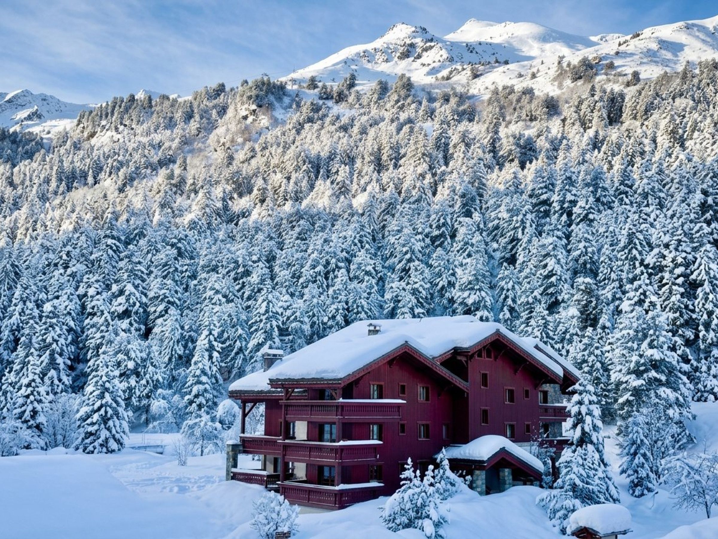 A multi-story building with a red facade, surrounded by snow-covered trees and mountains in the background.