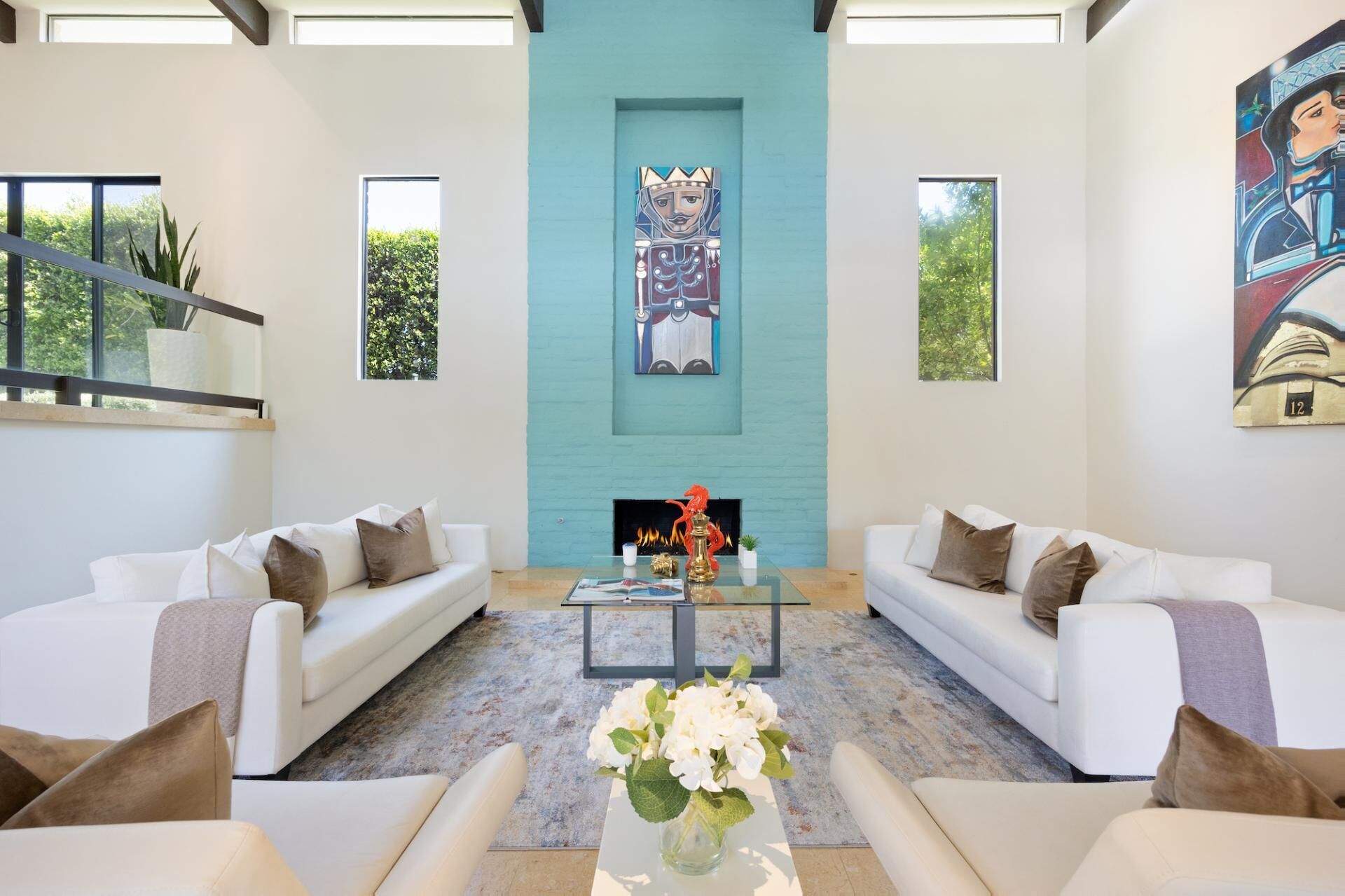 A spacious living room with a large fireplace, two white sofas, and a coffee table with a vase of flowers.