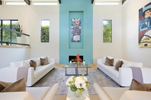 A spacious living room with a large fireplace, two white sofas, and a coffee table with a vase of flowers.