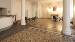 Un hall d’entrée spacieux, doté d’un sol en pierre polie, de colonnes blanches et de fauteuils verts disposés pour accueillir les visiteurs.