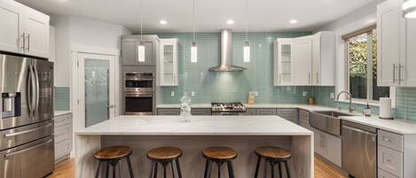 A modern kitchen with a central island, stainless steel appliances, and bar stools.